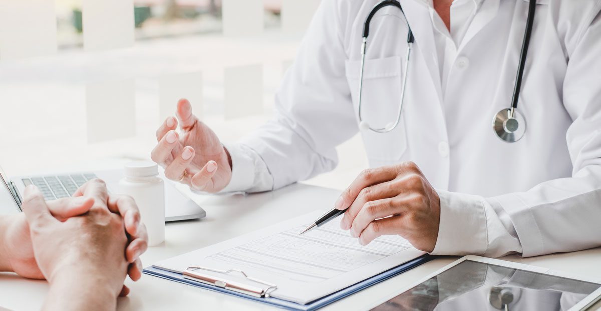 Doctor-consulting-patient-at-desk-with-clipboard-and-tablet Doctor-consulting-patient-at-desk-with-clipboard-and-tablet