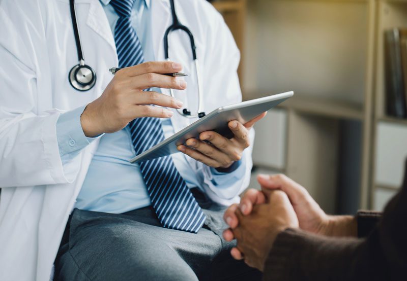 Doctor-consulting-with-patient-using-tablet-device Doctor-consulting-with-patient-using-tablet-device