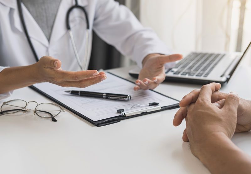 Doctor-discussing-treatment-with-patient-at-desk Doctor-discussing-treatment-with-patient-at-desk